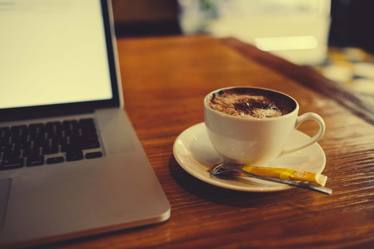A cup of cappuccino coffee or chocolate cacao in a white cup with laptop on table